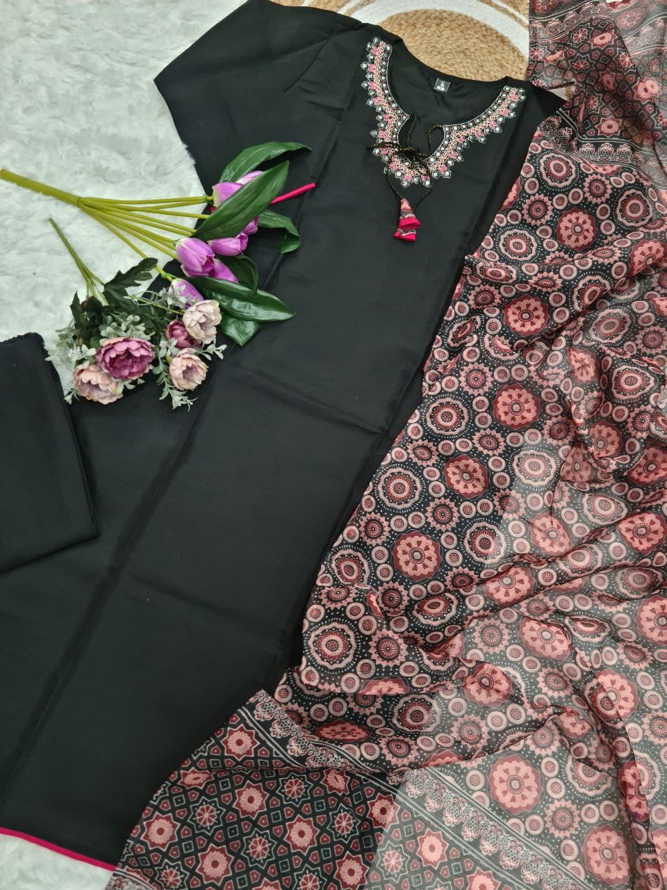 Black outfit with floral embroidery and a patterned scarf on a light background