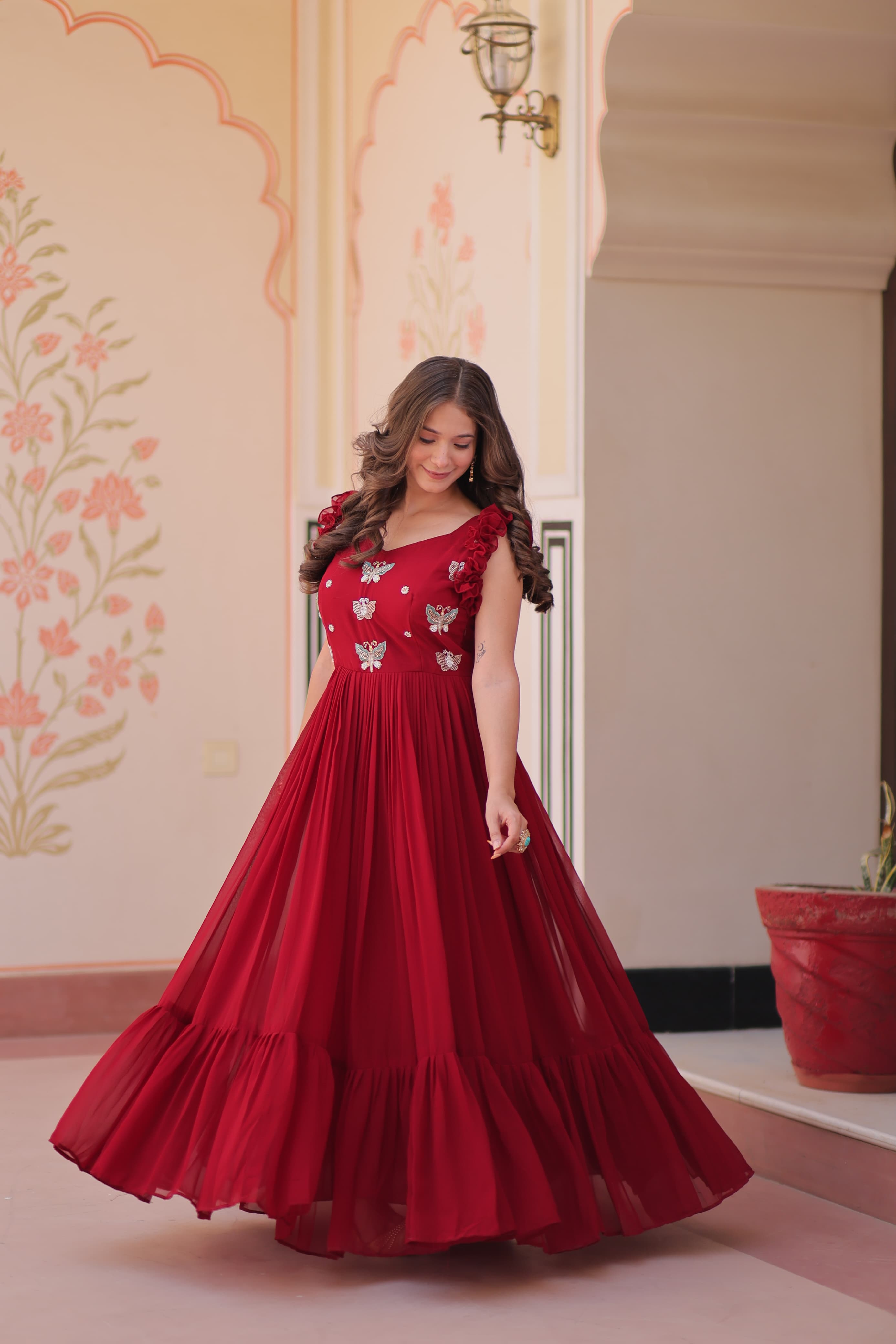 Woman in a red gown with floral patterns standing in an ornate room.