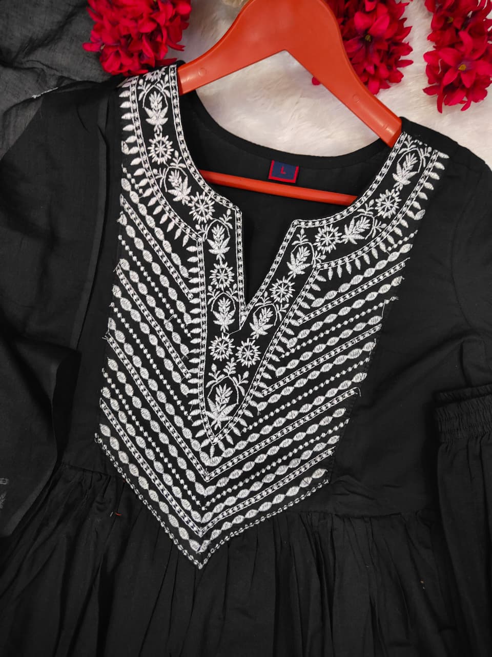 Black dress with white embroidery on a hanger against a floral background