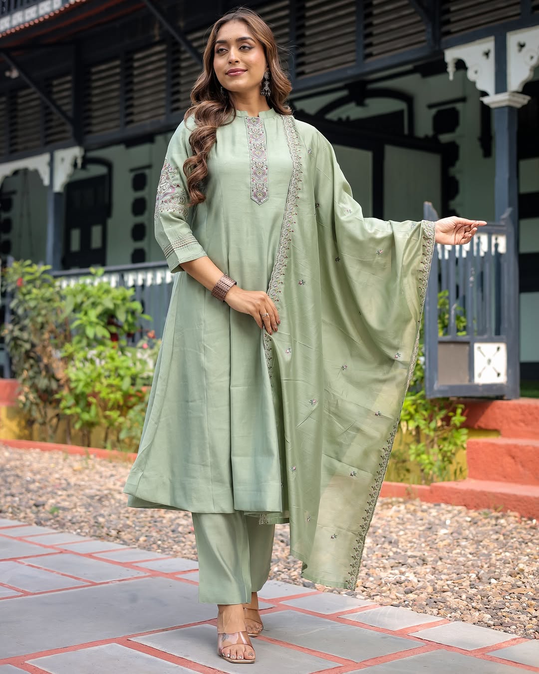 Woman wearing a light green traditional outfit with a dupatta, standing outdoors.