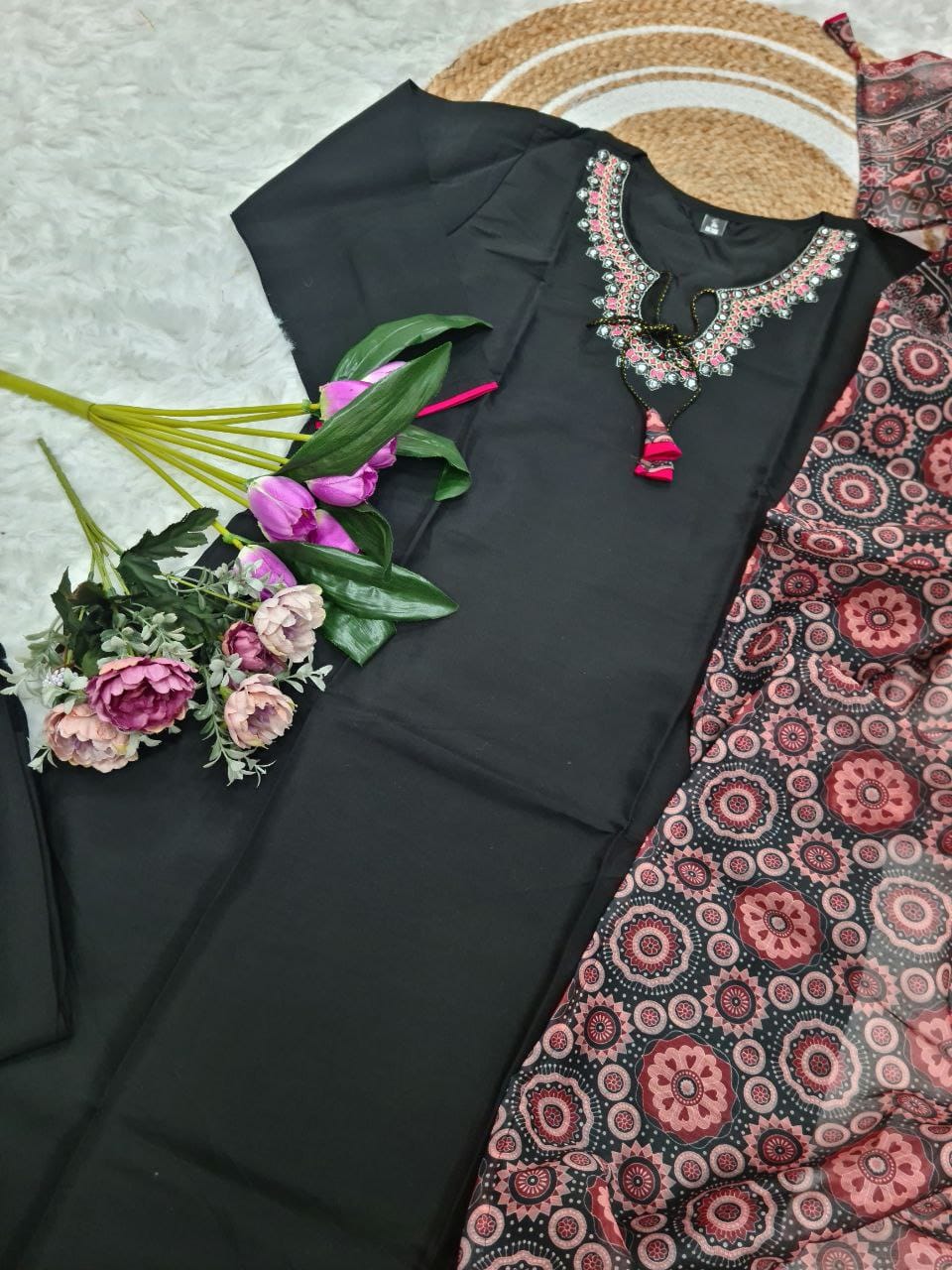 Black embroidered top with pink floral details on a patterned fabric background