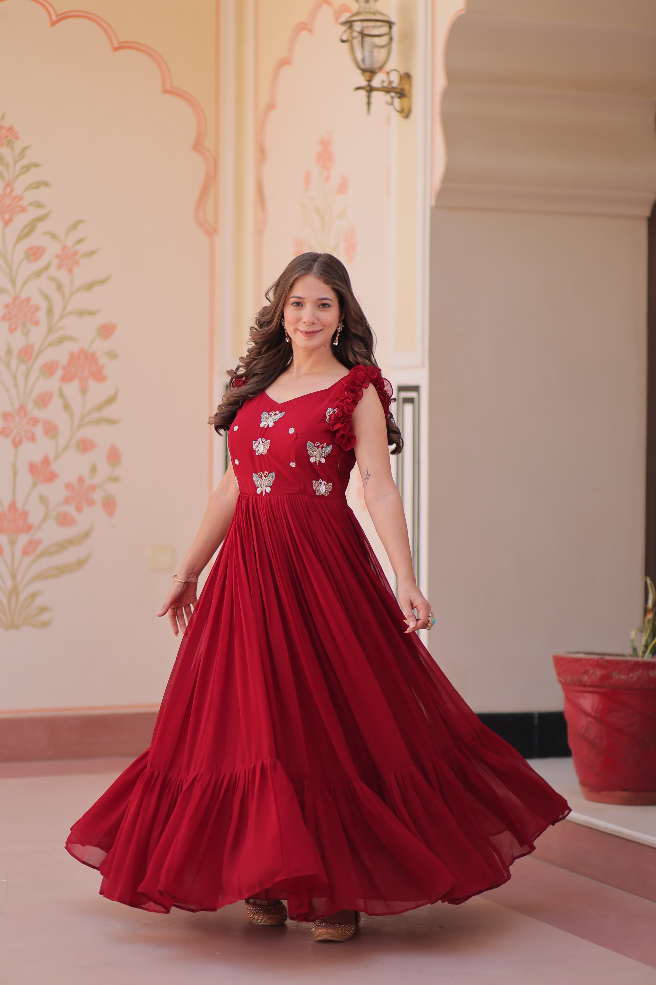 Woman in a red gown with floral patterns standing in an indoor setting.