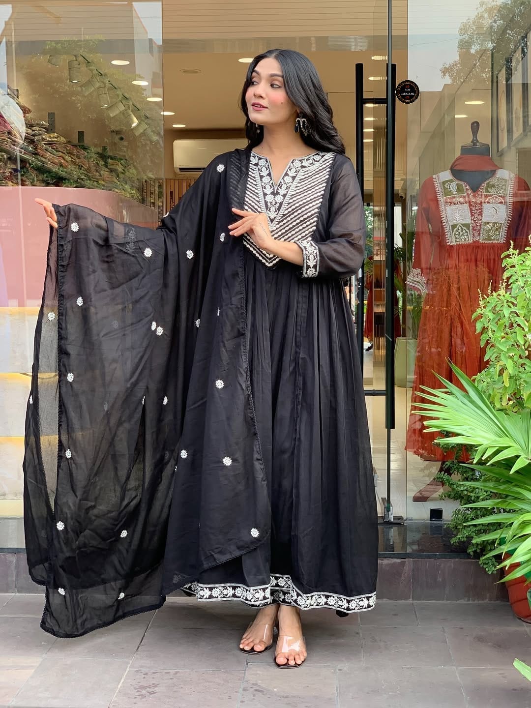 Woman in a black traditional outfit with white patterns standing in front of a store entrance.